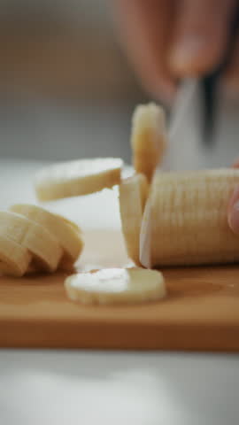 In a cozy kitchen setting, a pregnant woman carefully slices a fresh banana with a knife. The soft lighting highlights her focused expression as she prepares a healthy snack, showcasing daily life