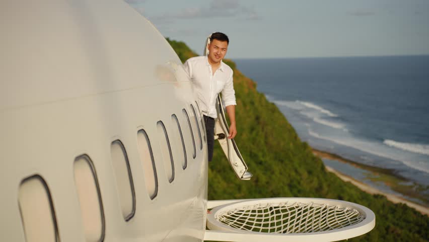 Successful asian man in unique hotel in Bali enjoys sea ocean view, the private villa made from airplane, traveling in Bali. Concept of success and freedom, big money. Pilot of aircraft on vacation 