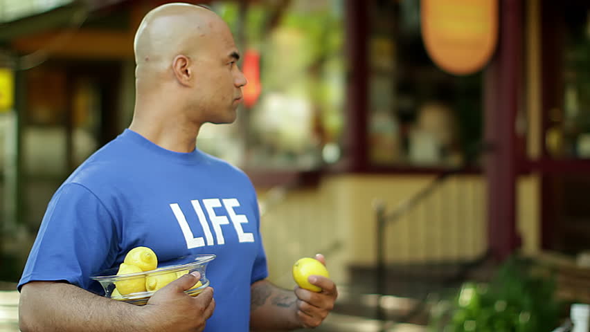 Man rips up a lemon after taking it from a guy in a blue T-shirt that says