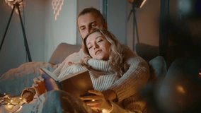 A couple sits comfortably on a couch, surrounded by soft lighting and decorations. They are engaged in reading, showcasing warmth and intimacy during a cold winter evening. - Powered by Shutterstock - Get 15% off with code: PIKWIZARD15