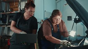 Two women mechanics collaborate inside a cluttered auto repair shop, inspecting a car while using a laptop for diagnostics. Their focus highlights teamwork and skill in the trade. - Powered by Shutterstock - Get 15% off with code: PIKWIZARD15