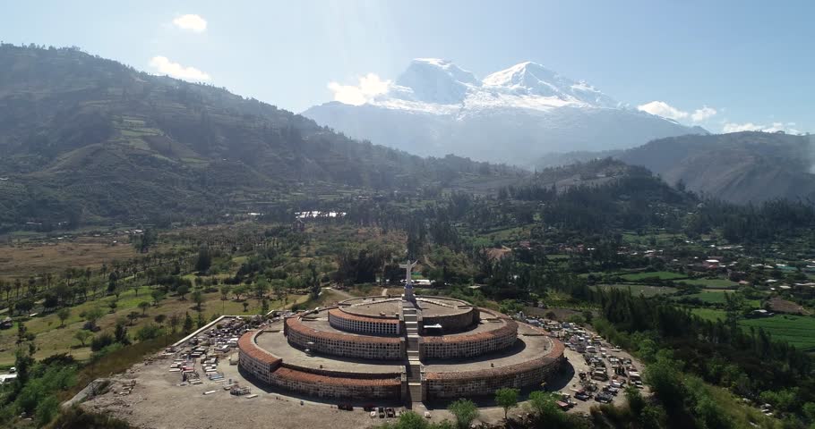 A breathtaking aerial view of the Yungay Cemetery in Áncash, Peru, featuring the Cristo monument and the towering Huascarán Mountain in the background.