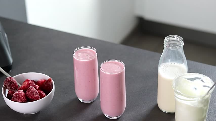 Close up of a woman in green sweater preparing fresh strawberries smoothie with yogurt and milk in the kitchen 