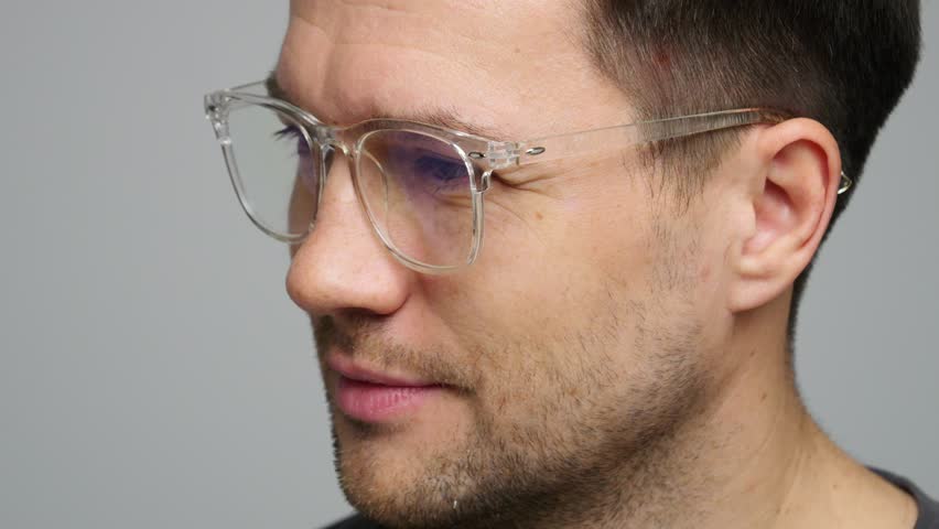 A genial young man casts a beaming smile against a neutral backdrop in an informal setting.