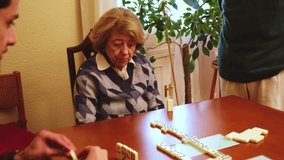 Elderly woman smiling while playing dominoes with her family, enjoying leisure time together - Powered by Shutterstock - Get 15% off with code: PIKWIZARD15
