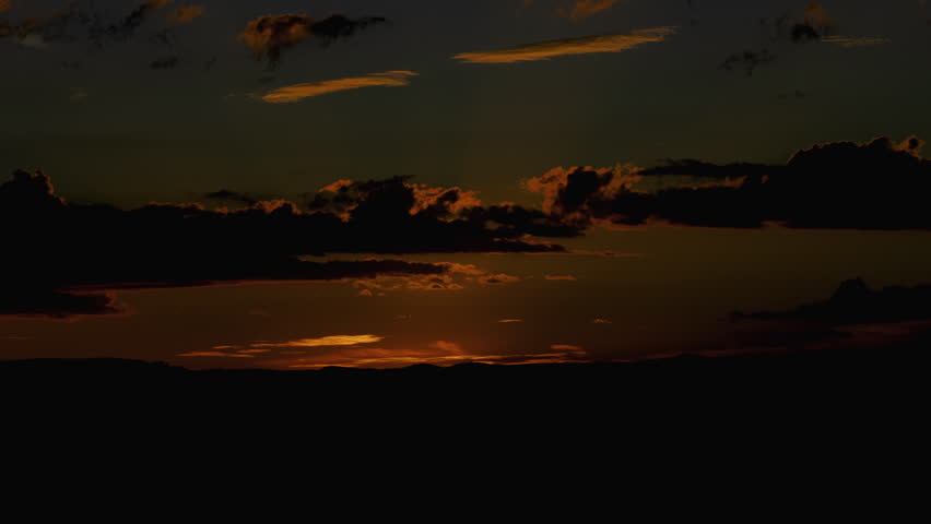 Golden desert sunrise timelapse as the sun rises above distant mountain ridgelines, casting radiant beams of light through scattered clouds. Warm amber and orange tones fill the sky while silhouetted terrain creates layered depth across the horizon.

Subtle cloud movement and shifting light add a cinematic quality, with sun rays breaking through gaps to create a glowing, atmospheric scene. The gradual transition from darkness to light emphasizes the beauty and stillness of the early morning desert.

Slow zoom in draws the viewer into the scene, making it ideal for establishing shots. Excellent for themes of dawn, renewal, nature, time passing, tranquility, and inspiration. Perfect for background footage, cinematic sequences, travel content, and motivational visuals.

Concepts include sunrise, desert landscape, timelapse, sun rays, clouds, horizon, mountains, silhouette, golden hour, morning light, atmosphere, scenic, Southwest, nature, peaceful, and 4K footage.