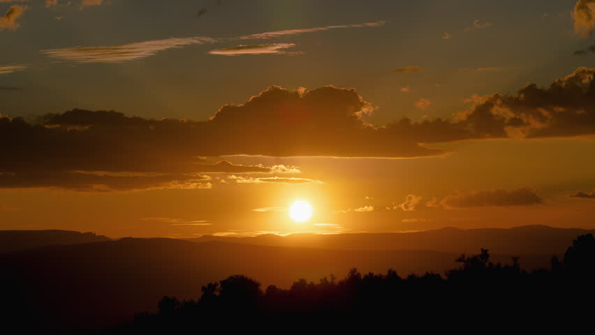 Golden desert sunrise timelapse as the sun rises above distant mountain ridgelines, casting radiant beams of light through scattered clouds. Warm amber and orange tones fill the sky while silhouetted terrain creates layered depth across the horizon.

Subtle cloud movement and shifting light add a cinematic quality, with sun rays breaking through gaps to create a glowing, atmospheric scene. The gradual transition from darkness to light emphasizes the beauty and stillness of the early morning desert.

Slow zoom in draws the viewer into the scene, making it ideal for establishing shots. Excellent for themes of dawn, renewal, nature, time passing, tranquility, and inspiration. Perfect for background footage, cinematic sequences, travel content, and motivational visuals.

Concepts include sunrise, desert landscape, timelapse, sun rays, clouds, horizon, mountains, silhouette, golden hour, morning light, atmosphere, scenic, Southwest, nature, peaceful, and 4K footage.