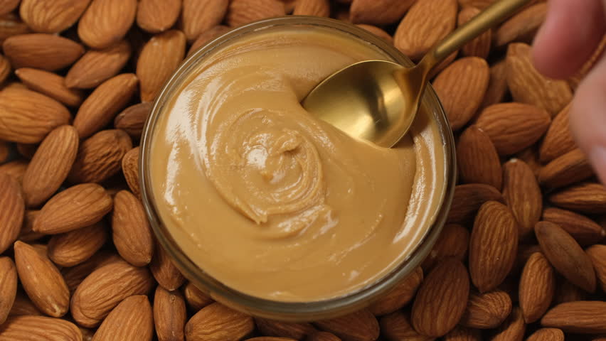 Almond butter scooping with golden spoon. Creamy smooth almond butter and whole almonds
