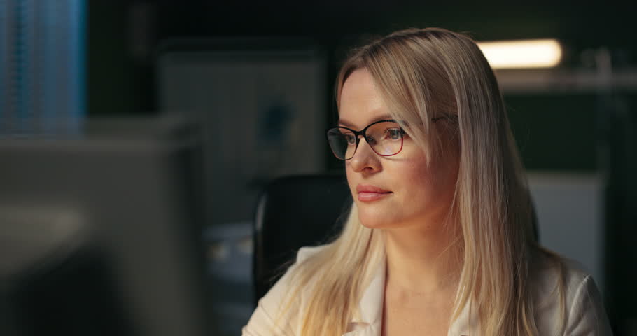 A woman wearing fashionable glasses is working diligently and focused at her desk.