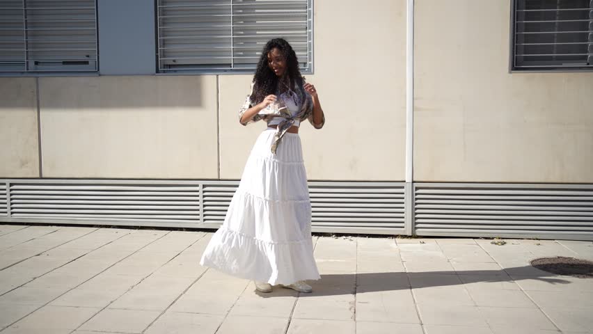A joyful dancer clad in a beautifully flowing white dress performs with grace and elegance outdoors, showcasing her artistic talent and freedom against a simple and minimalistic backdrop