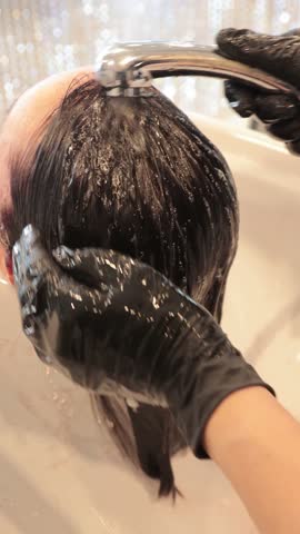 Hairdresser lathering shampoo into client's wet hair at hair salon