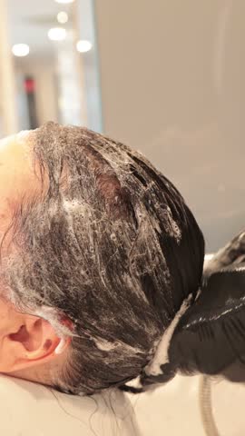 Hairdresser lathering shampoo into client's wet hair at hair salon