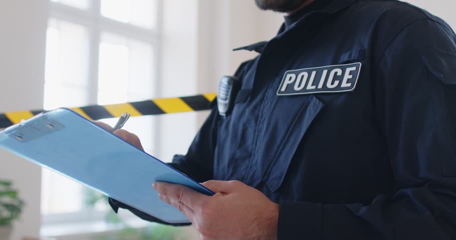 Closeup of a male policeman or detective collecting evidence and preparing a report, writing on tablet at a crime scene. Law enforcement focus on security and detailed investigations.