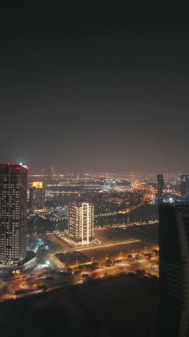 The skyline of the Lusail area from top in Doha, Qatar. Illuminated modern skyscrapers aerial view from rooftop at night. Parks and traffic on the road.