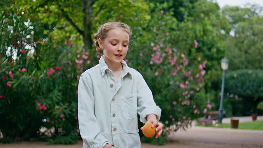 Little girl playing tennis at green park closeup. Blonde small child holding rocket and ball enjoying favourite sport at lush urban garden. Joyful sportive kid feeling active relaxing at fresh air