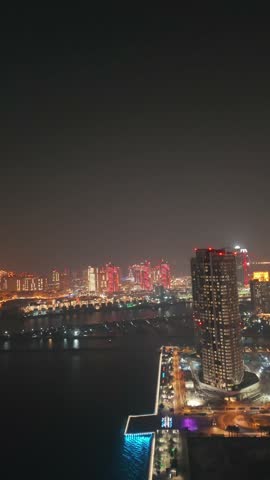 The skyline of the Lusail area from top in Doha, Qatar. Illuminated modern skyscrapers aerial view from rooftop at night. Parks and traffic on the road.