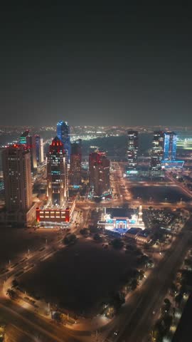 The skyline of the Lusail area from top in Doha, Qatar. Illuminated modern skyscrapers aerial view from rooftop at night. Parks and traffic on the road.