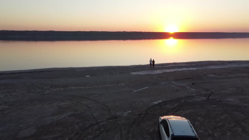 Aerial video of a couple (man and woman) watching a beautiful sunset near a mirror lake