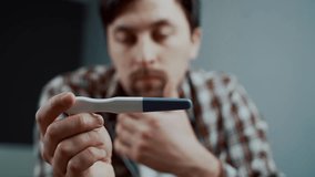 A man gazes at the pregnancy test his wife gave him, holding his head in distress. His expression reveals worry and disappointment, clearly showing that the unexpected pregnancy is unwelcome to him - Powered by Shutterstock - Get 15% off with code: PIKWIZARD15