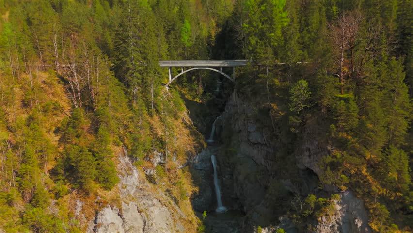 Luftaufnahme Schurpfen Wasserfall. Aerial view of crooked waterfall Schurpfen and bridge in gorge with forested mountain and canyon near Sylvensteinspeicher in Lenggries. Drone view falls and bridge. 