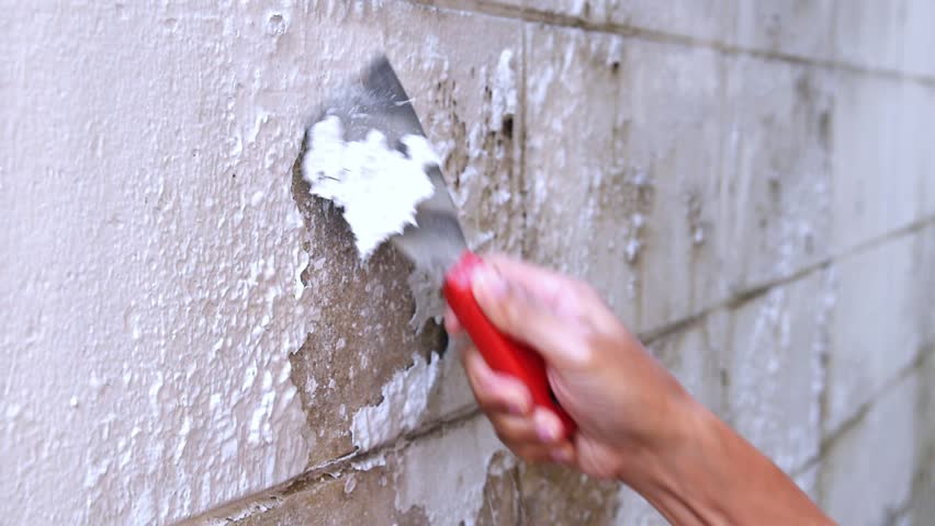hand holding putty knife scraping weathered paint layer peeling off on wall, constructor using spatula to scrape off damaged paint, preparation for repair, renovation, repainting or home improvement - Powered by Shutterstock - Get 15% off with code: PIKWIZARD15