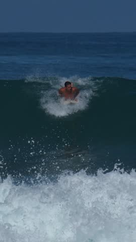 Young male adult surfs in the blue ocean at sunny day