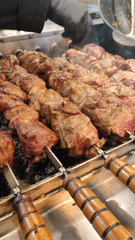 Frying shashlik. Grilling kebabs on mangal. Pieces meat roasting on rotating skewers over coals. Delicious grilled meat on spinning skewer. Cooking meat food BBQ. Cooking street food barbecue Vertical