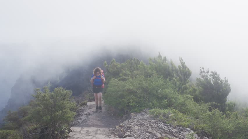 A woman explores the beautiful landscape of Laurisilva in Garajonay National Park. The mist envelops the lush greenery, as trade winds push clouds against the forest creating a serene atmosphere.