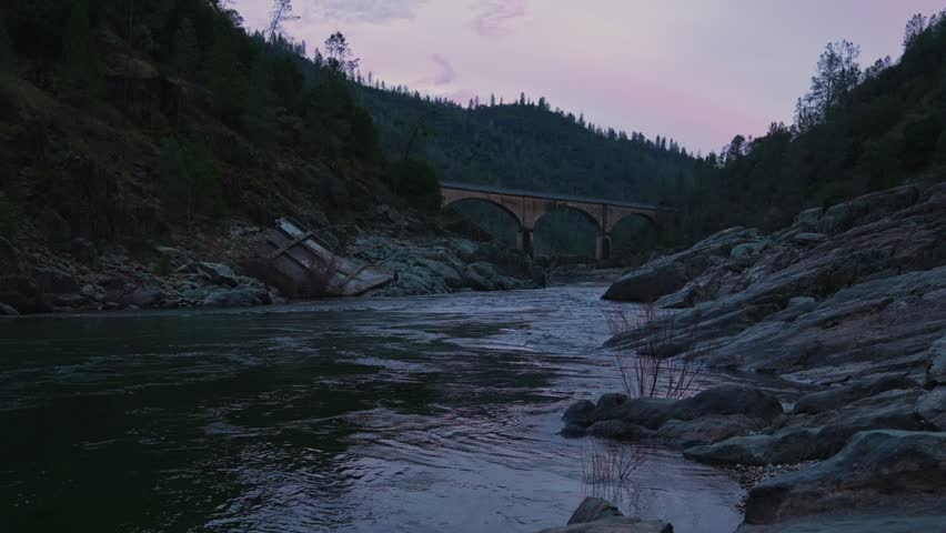Twilight River with Historic Arched Bridge and Rocky Shore