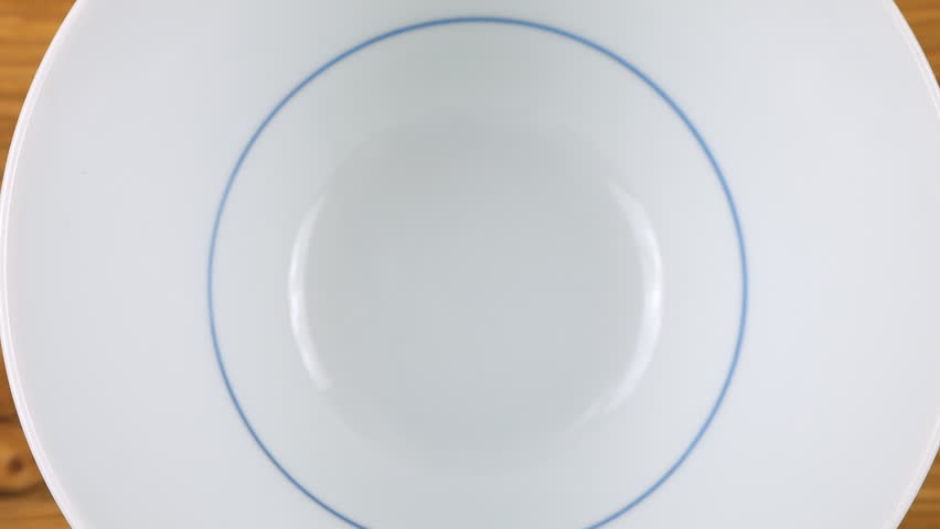 Salad seed mix is ​​poured into a white ceramic bowl. Sesame, flax, caraway, sunflower and pumpkin seeds. Top view. Slow motion.