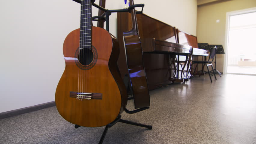 Acoustic guitars rest closely together demonstrating intricate woodwork. Vibrant atmosphere of music class promises creativity and learning