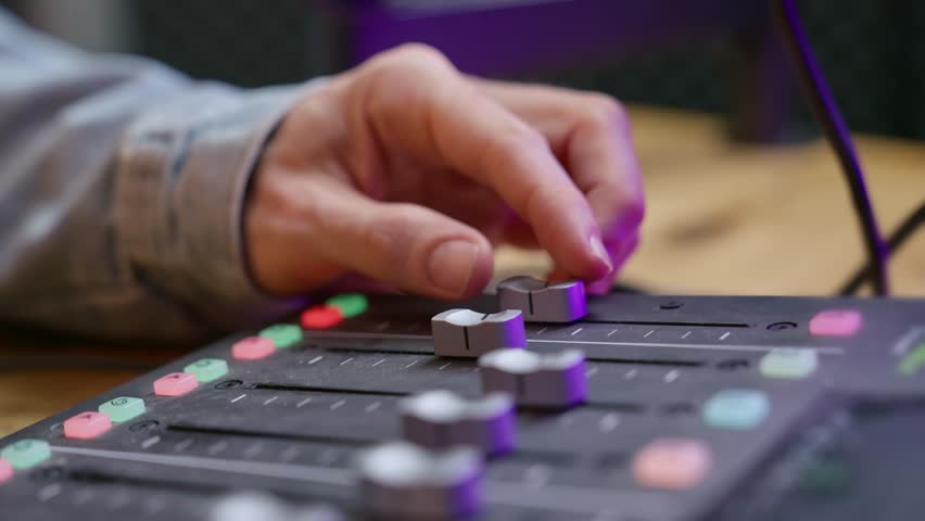 Close up on podcast sound console or audio recording mixer - man's hand pressing buttons and moves switches and faders in professional studio getting ready for live streaming session or radio show