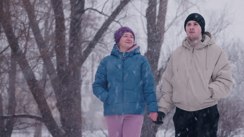 Young couple standing hand in hand, looking into the distance as light snowfall creates a picturesque winter scene around them. High quality 4k footage