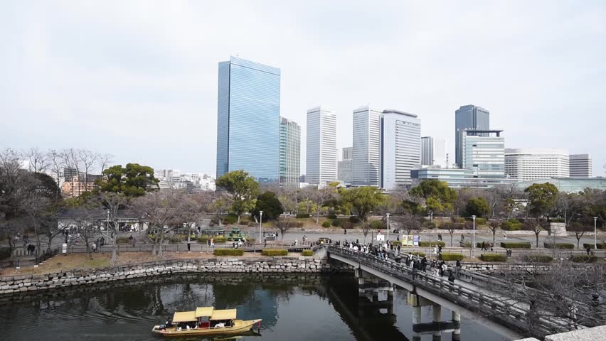 Traditional rowing boat in the waters of the inner Castle moat. Passing under the Gokuraku-bashi Bridge . Osaka Castle, Japan. Skyline of Osaka Buisness Park in the background.
