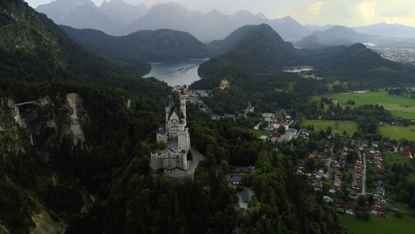 Beutiful aerial around the famous castle Neuschwanstein front revealing the alp mountains behind it and castle Hohenschwangau + lake Alpsee in the background