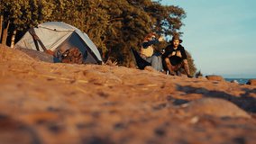 Camping on picturesque beach, town tourists relaxing on shore after hike, halt. Happy young adult people enjoying summer vacation, spending time together in nature, drinking hot tea from thermos - Powered by Shutterstock - Get 15% off with code: PIKWIZARD15