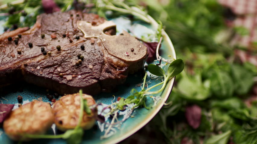 Grilled T-Bone Steak Rotating on Table with Fresh Greenery