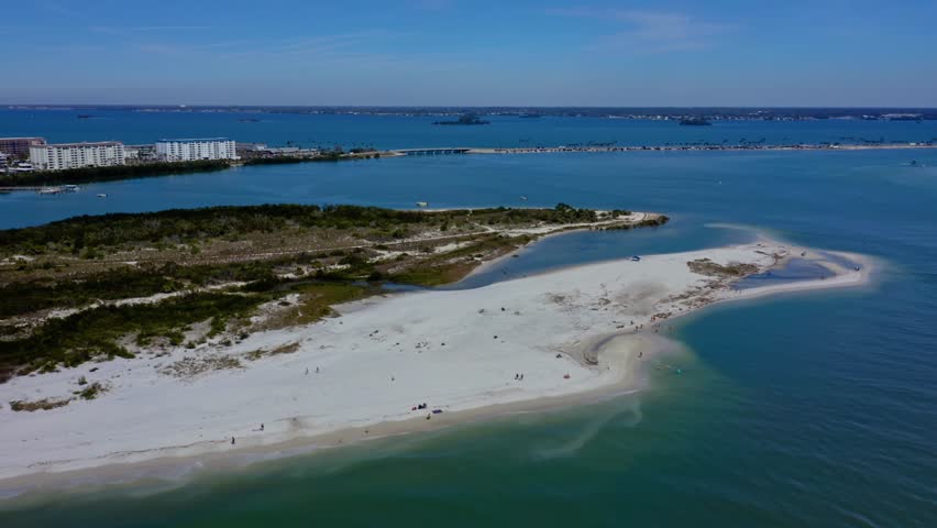 A stunning sandbar extends along the shoreline of Honeymoon Island, Florida, surrounded by calm turquoise waters. The aerial perspective showcases the island’s coastal dunes and natural beauty.