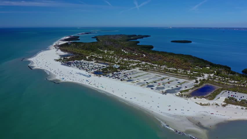 Honeymoon Island, Florida, showcases a vast sandy beach, clear turquoise waters, and a lush green landscape. The aerial perspective captures the island’s shoreline, parking lots, and nature.