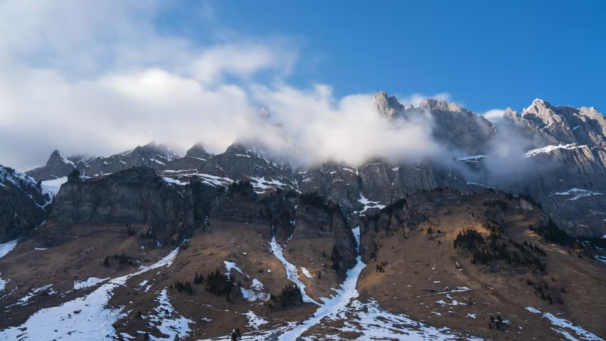 Mountain ranges switzerland. the mountain peaks are snow covered and the sun rays shine through the clouds. the clouds swirl at the peaks. Beautiful swiss landscape. Timelapse. Pure nature