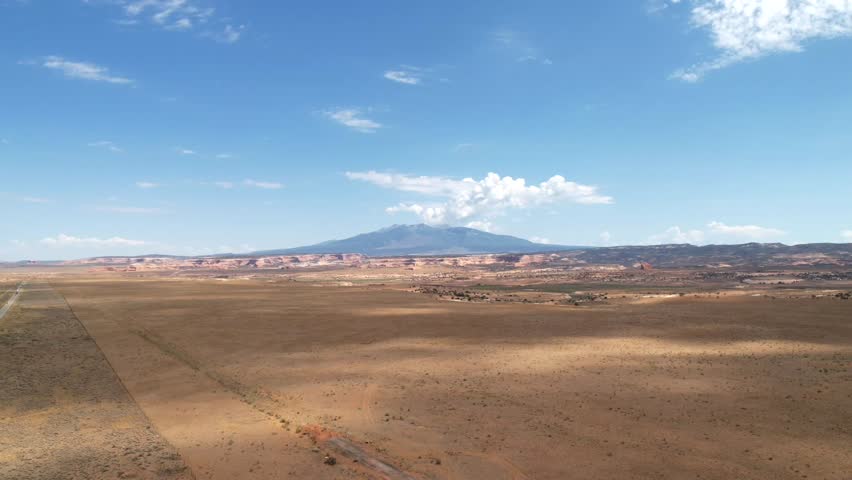 Timelapse Drone Flight: Gliding Over Sand and Rock Terrain with Fast-Moving Clouds and Mountains on the Horizon