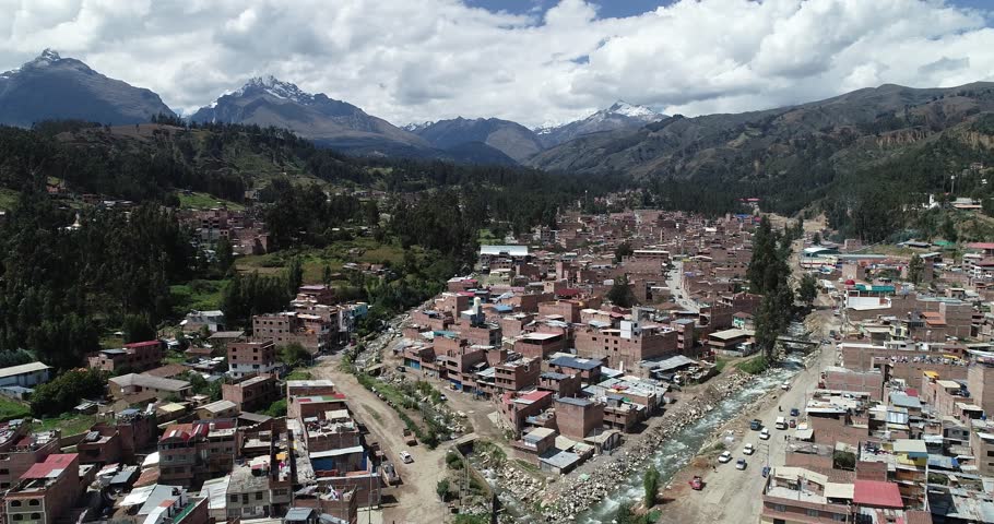 Drone shot of Huaraz, a vibrant Andean city in Peru, surrounded by towering mountains, rustic brick houses, and a flowing river. Ideal for travel, culture, and documentary content