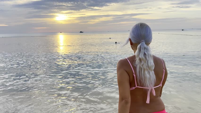 A girl enters the sea. Evening. The sun will soon set behind the horizon. The water is calm and quiet. There are no waves at all. A paradise for relaxation. Vietnam. South China Sea.
