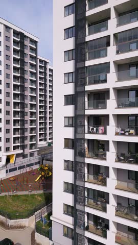 Modern residential apartment buildings with glass balconies and a playground below. The urban housing complex features contemporary architecture, outdoor living spaces, and a well-maintained communal