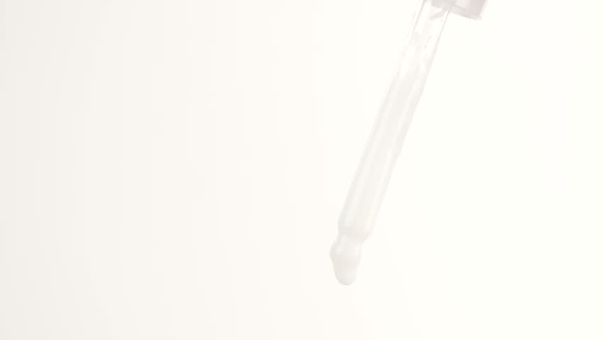 Drops of white serum falling from a glass pipette.