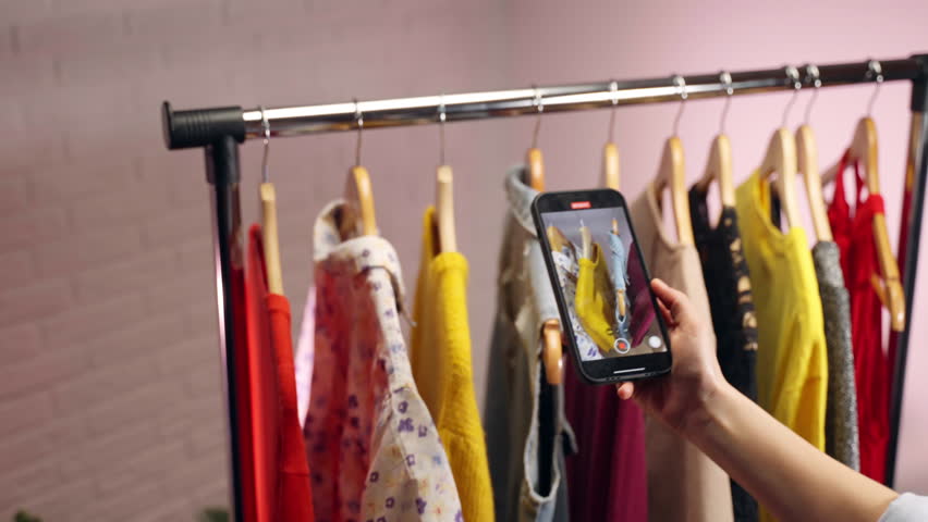 Process of social media content creation in fashion boutique, female influencer recording videos of exclusive apparel from new collection on smartphone, creativity and startup in fashion business