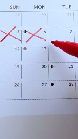 Signing a day on a calendar. Crossed out dates with red marker on calendar.