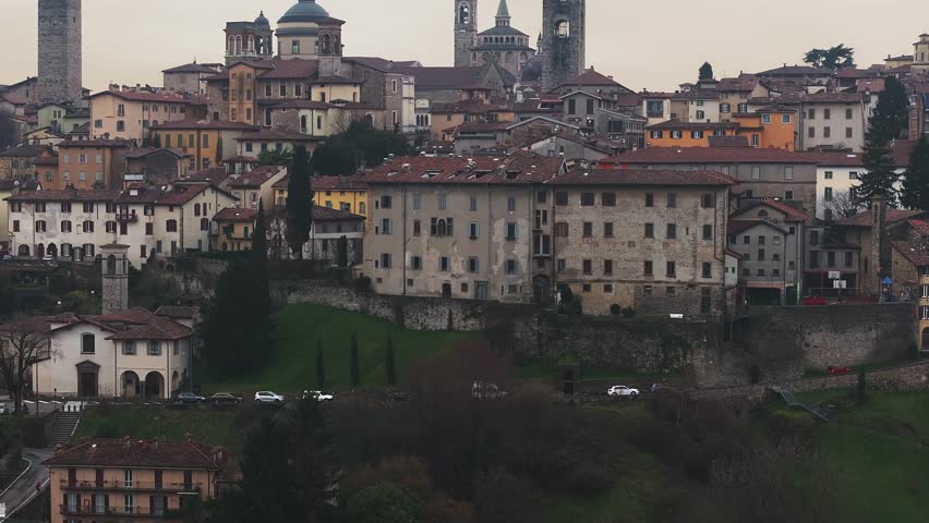 View of Bergamo's old town in Italy as the setting sun transitions, illuminating the Campanone, Basilica, and terracotta rooftops with warm hues.