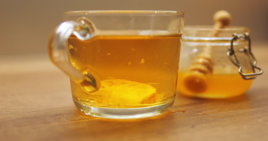 Slice of lemon sinks to bottom in tea cup contributing to sour flavor of drink. Beverage with citrus against honey jar maintains hydration and essential nutrients