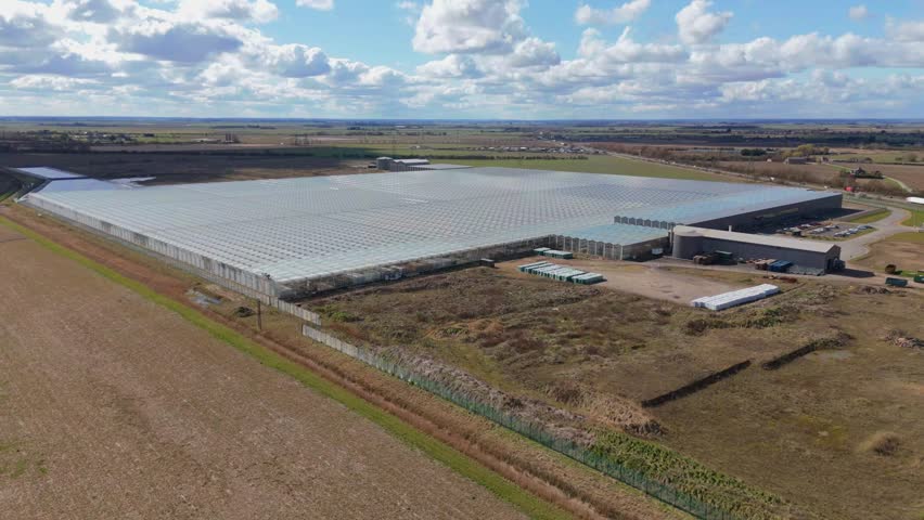 Aerial view of large data centre processing facility glass building expansive countryside flat agricultural land quantum farming sunny day England UK Europe.